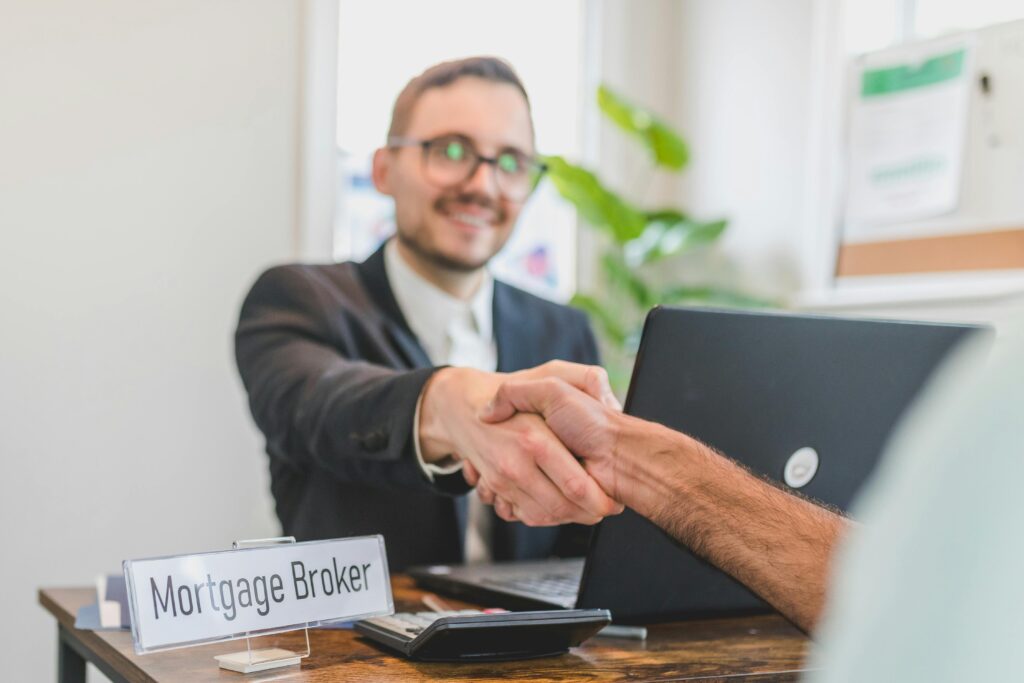 Mortgage broker and client sealing a deal with a handshake in a bright, modern office.
